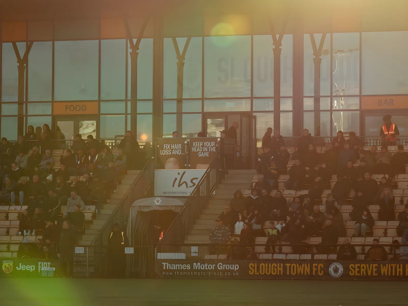 Supporters in the stand at Arbour Park as the sun sets